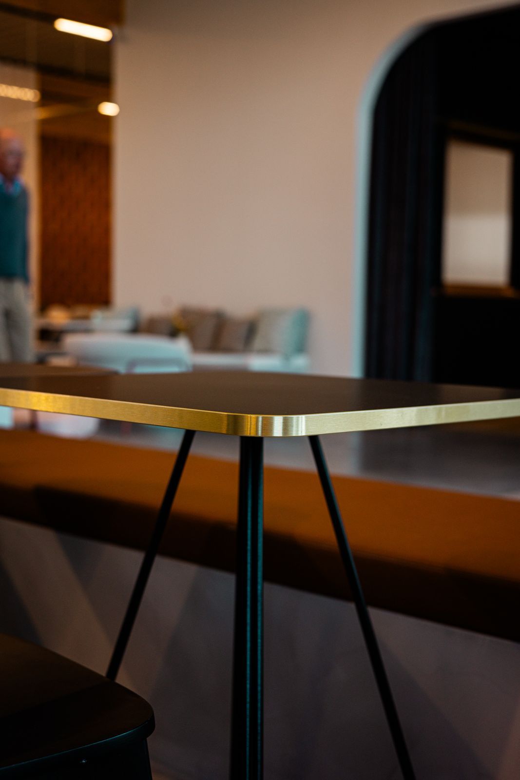 Plateau rectangulaire noir avec chant doré sur un piètement noir à trois pieds, dans un lounge