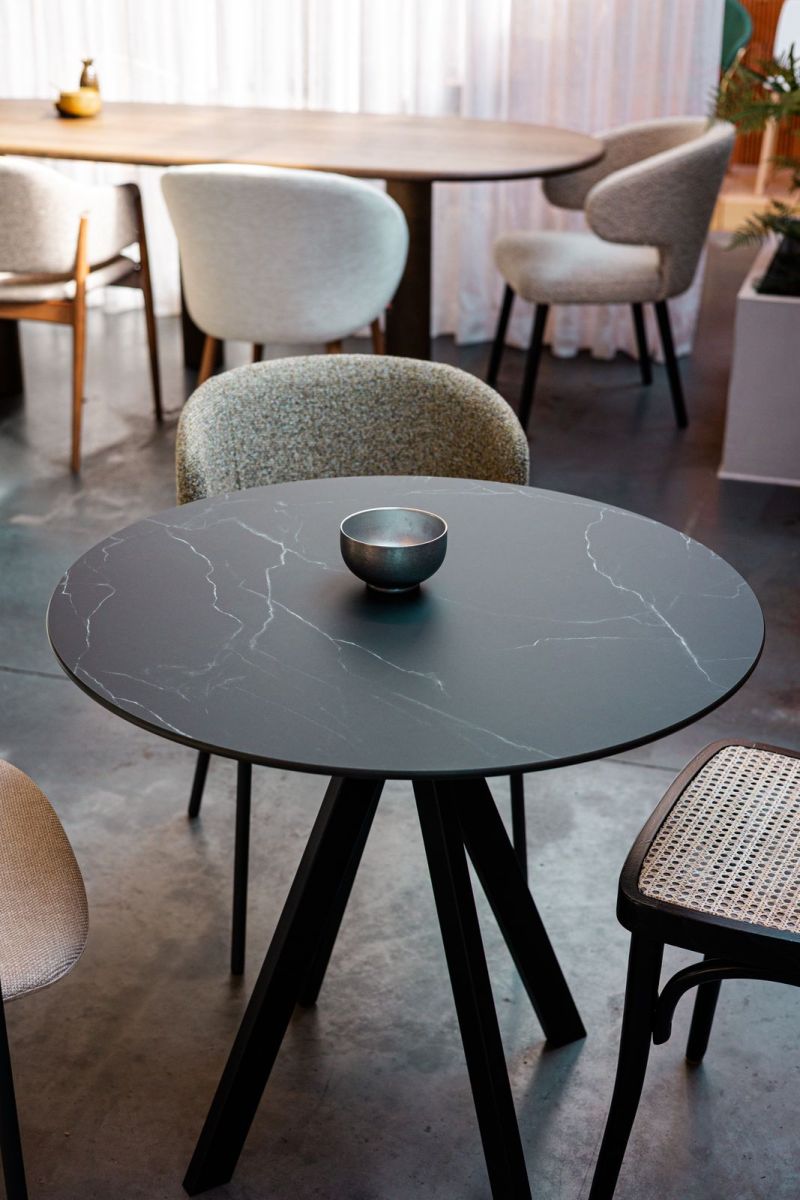 Plateau rond en décor marbre noir sur un piètement à trois pieds, avec une table ovale à l'arrière-plan
